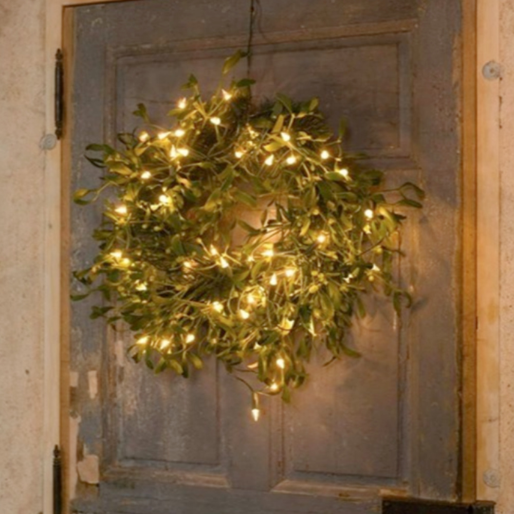 Holiday mistletoe wreath with white lights on a rustic weathered door in France - @loirevalleycooking. #frenchcountrychristmas #christmaswreaths