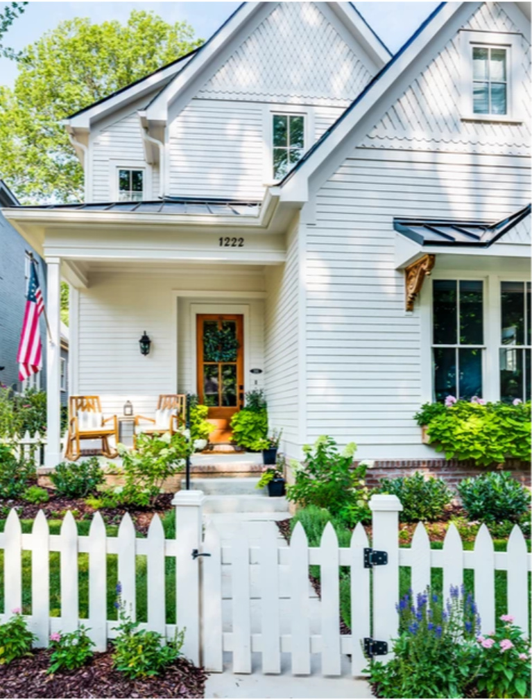 Darling Victorian home with front porch, picket fence, and American flag - Garden Gate Homes. Come peek at Charming Porch Inspiration & Decor Ideas. #homeexteriors #housedesign #victorianhomes #frontporch #curbappeal