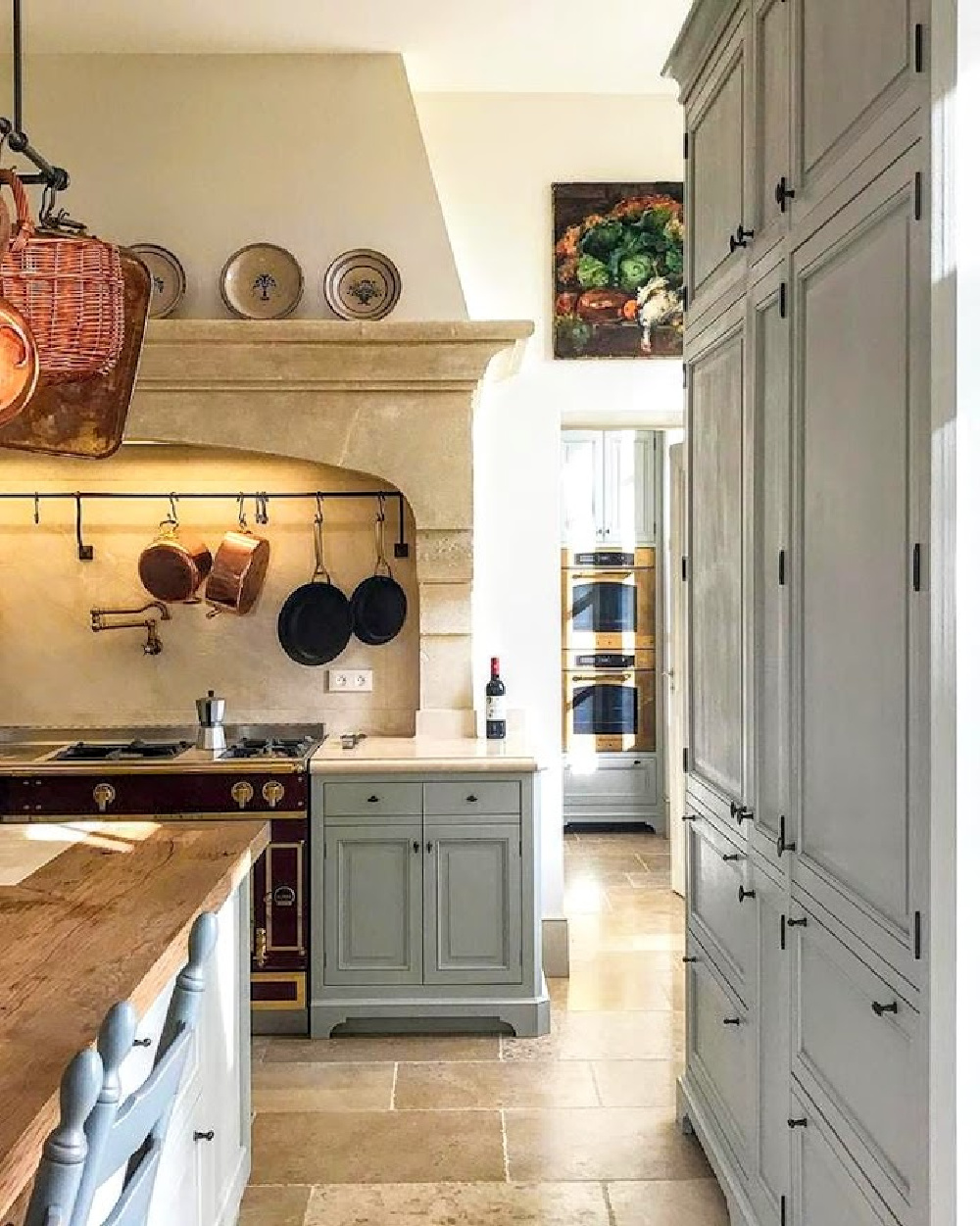 French farmhouse kitchen with copper pans on rack, light blue cabinetry, and stone floors - Le Mas des Poiriers.