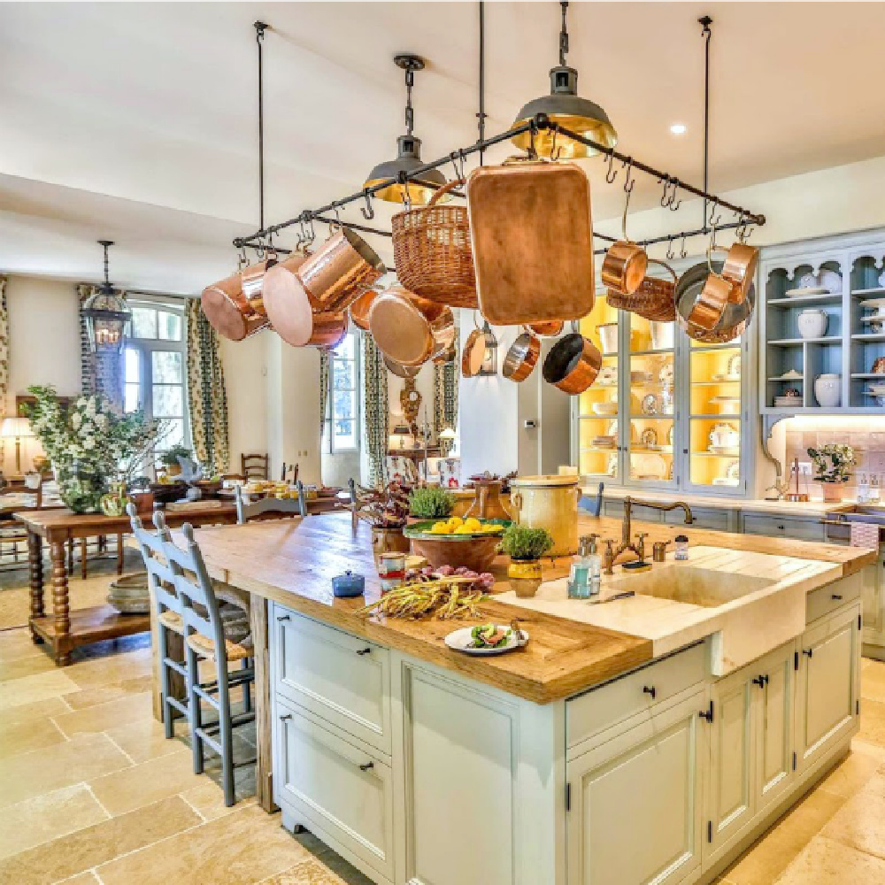 French farmhouse kitchen with copper pans on rack, light blue cabinetry, and stone floors - Le Mas des Poiriers.