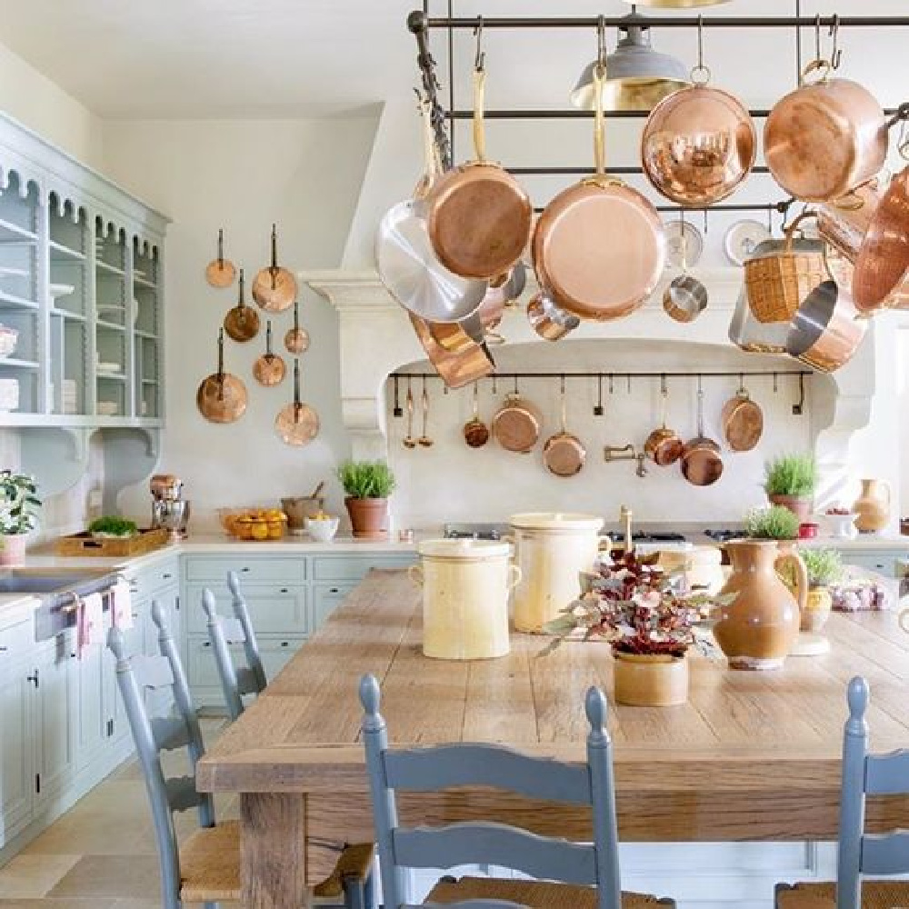 French farmhouse kitchen with copper pans on rack, light blue cabinetry, and stone floors - Le Mas des Poiriers.