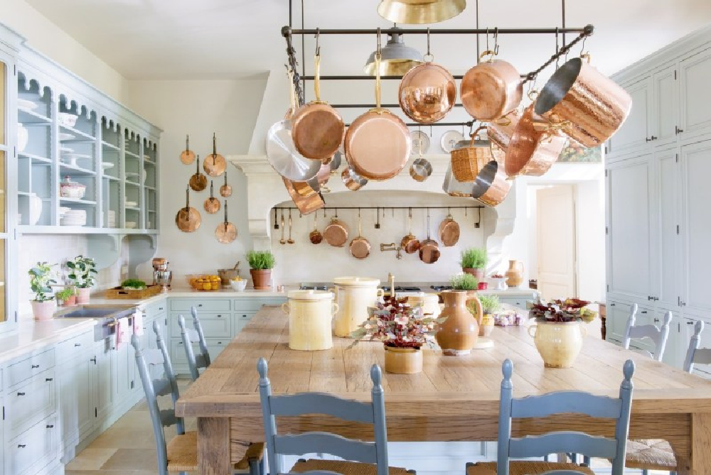 French farmhouse kitchen with copper pans on rack, light blue cabinetry, and stone floors - Le Mas des Poiriers.