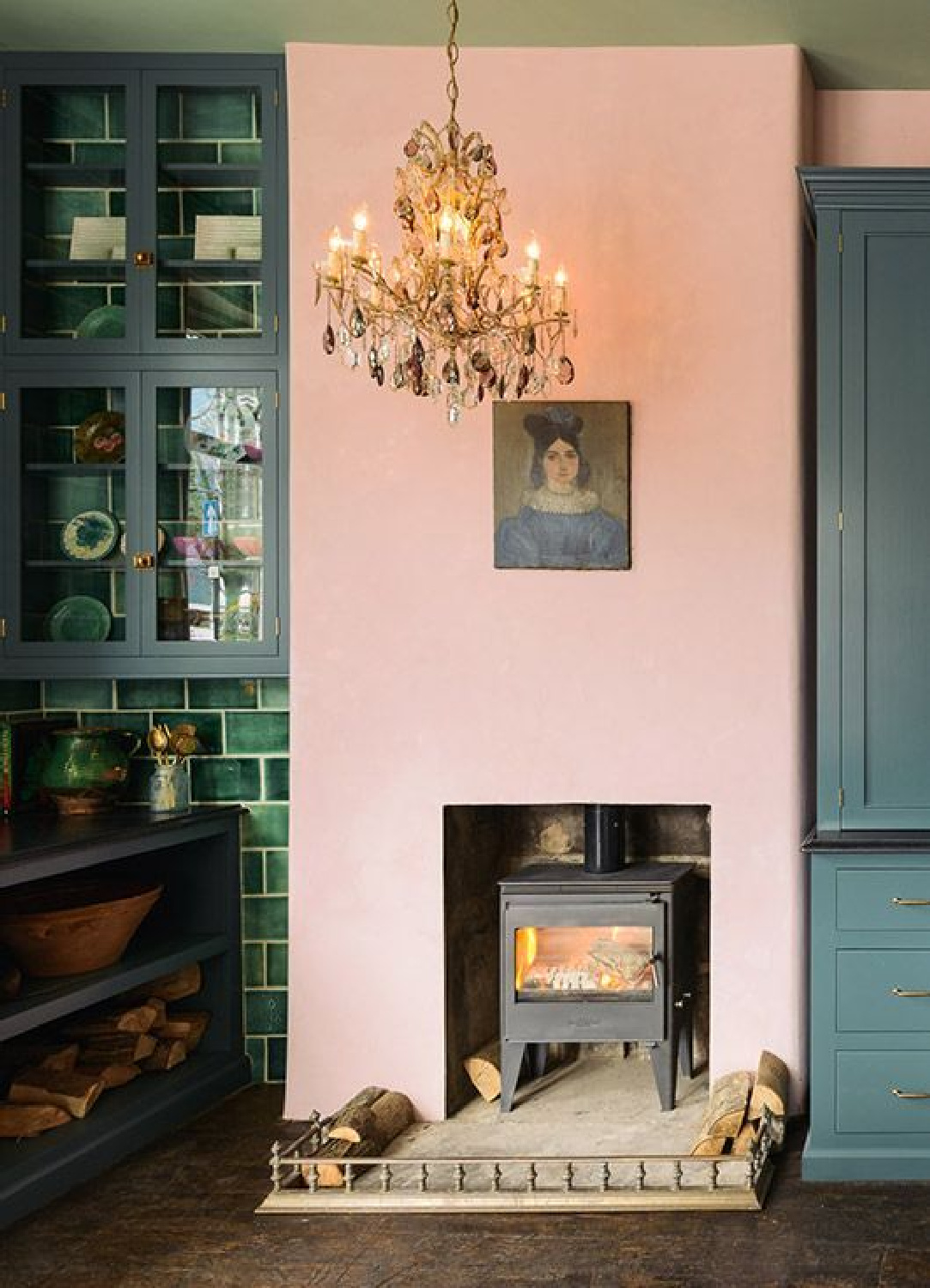 Pink plaster walls surround a woodstove in an English country kitchen by deVOL with green cabinets and tile. Not sure how to work blush into your home? See this story on Hello Lovely Studio!