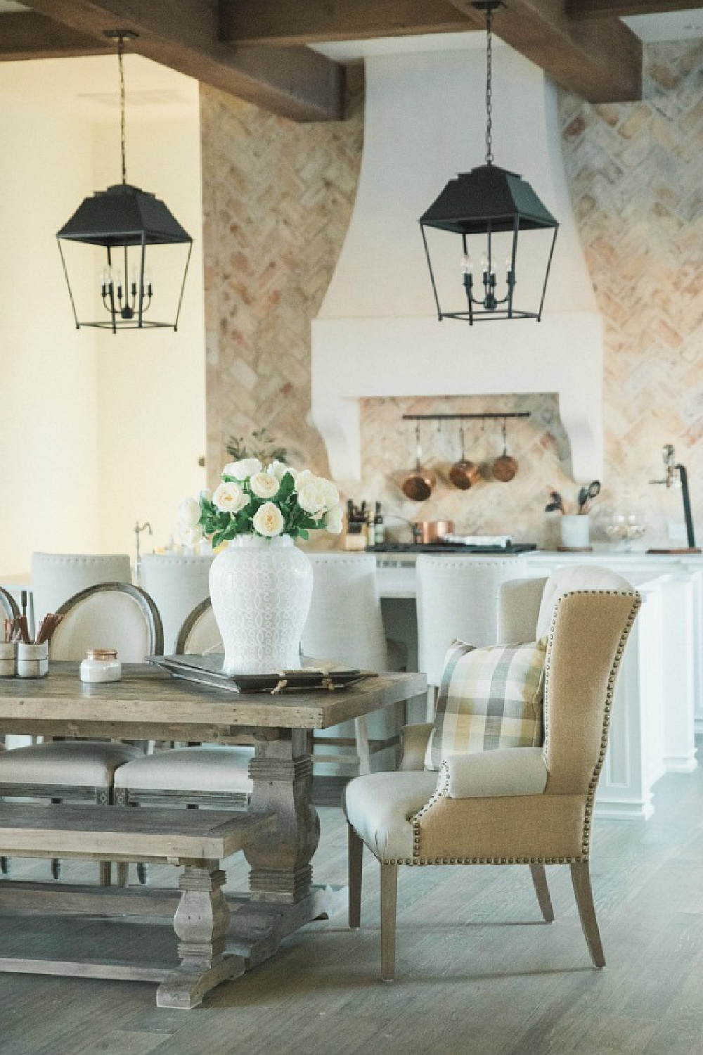 French country farmhouse kitchen with rustic lanterns, farm table, wing chairs, reclaimed Chicago brick, and Sherwin Williams Alabaster white paint on walls. Brit Jones Design. See more Gorgeous European Country Interior Design Inspiration on Hello Lovely. #europeancountry #frenchfarmhouse #interiordesign