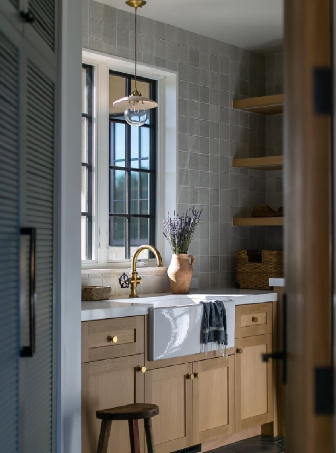 Beautiful classic laundry room with farm sink, windows, wood cabinets, open shelves, and brass hardware - @blackbanddesign #laundryroomdesign