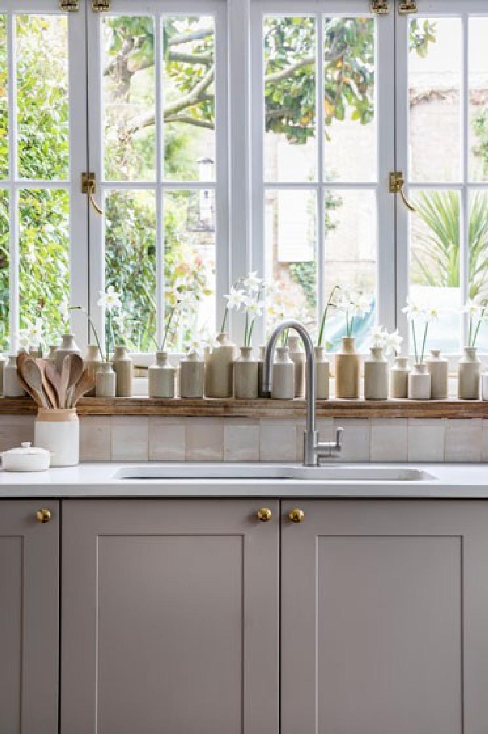 Modern farmhouse classic kitchen with grey cabinets, zellige tile backsplash, and a collection of putty colored stone English pottery lined up on the window sill. Interior Design by Imperfect Interiors. Photo: Chris Snook. #kitchendesign #modernfarmhouse #englishpottery #vintagestyle #slowliving #greycabinets