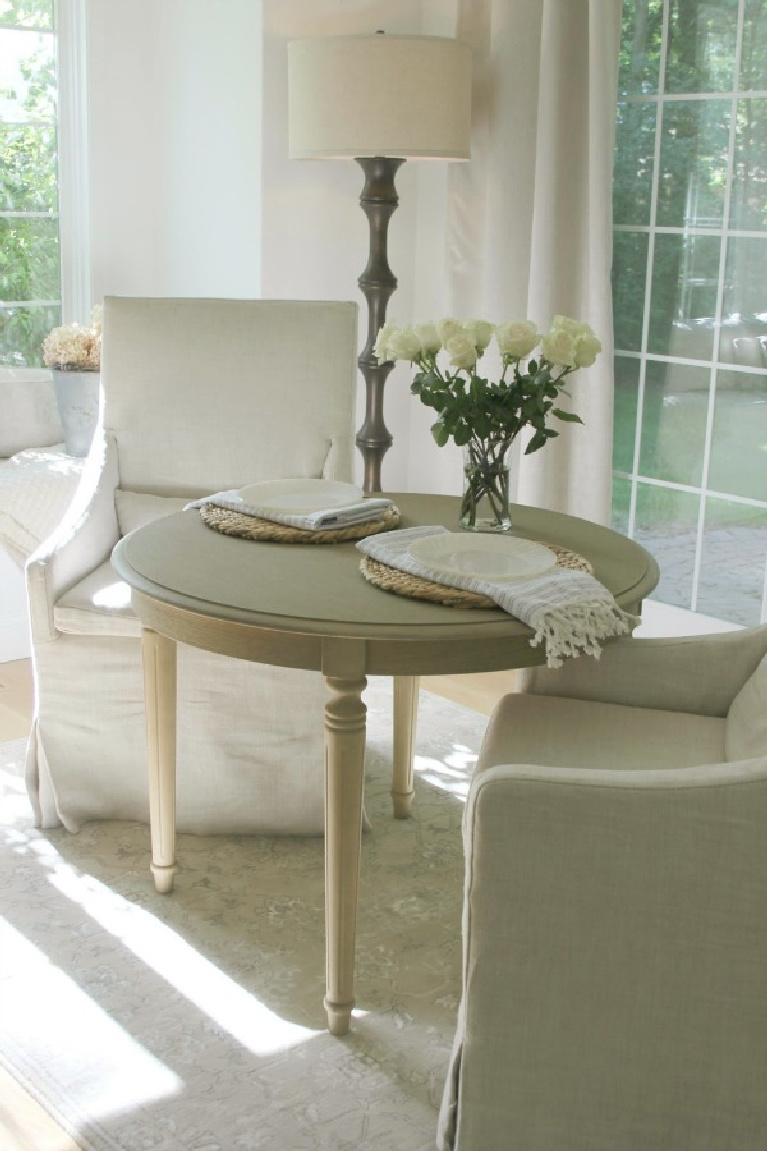 Belgian linen slope arm dining chairs and small round breakfast table in serene kitchen - Hello Lovely Studio. #frenchcountry #nordicfrench #belgianlinen #breakfastnook #slopearmchairs #serenedecor