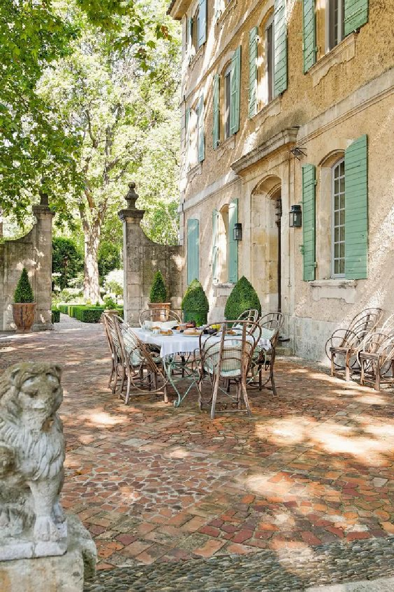 Cheerful green shutters on warm sunny-hued stucco Chateau Mireille in Provence. #frenchchateau #frenchhome #houseexterior #shutters #outdoordining #southoffrance #vacationvilla #provence