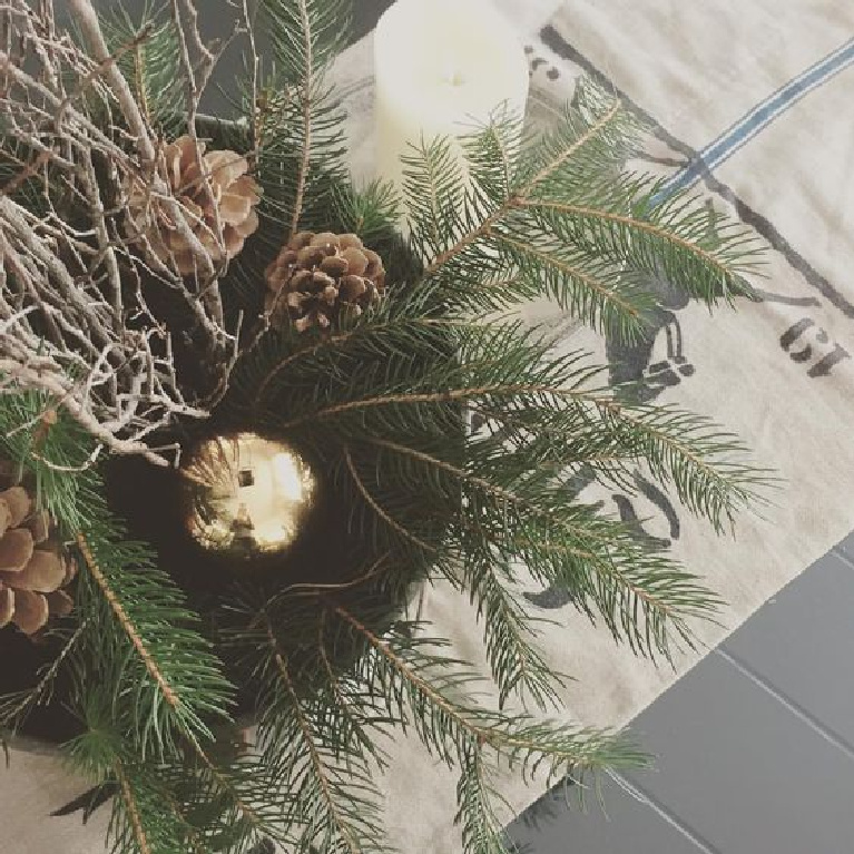 Simple Christmas decor with a European Country feel from Hello Lovely Studio with fresh greenery and pinecones in a farmhouse bucket set upon an antique German grainsack. #christmasdecor #holidaydecorating #hellolovelystudio #christmasgreenery #oldfashionedchristmas #eurochristmas