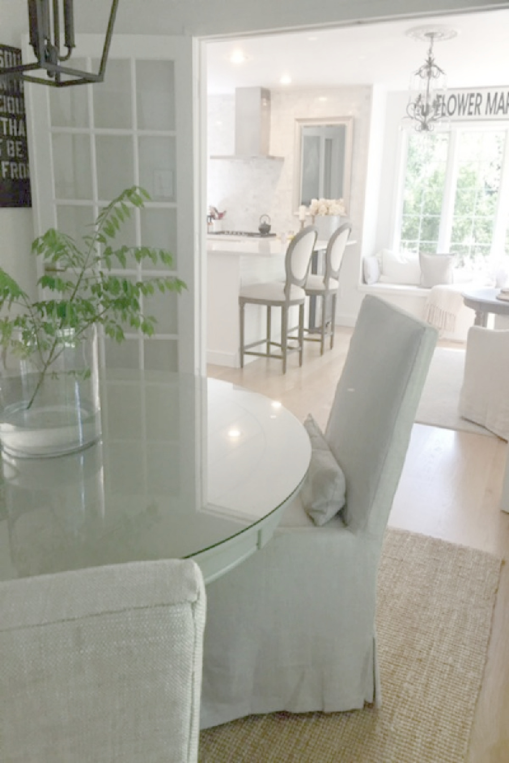 Serene dining room with linen slipcovered chairs, round table, French doors to kitchen, and white oak hardwood floors - Hello Lovely Studio.