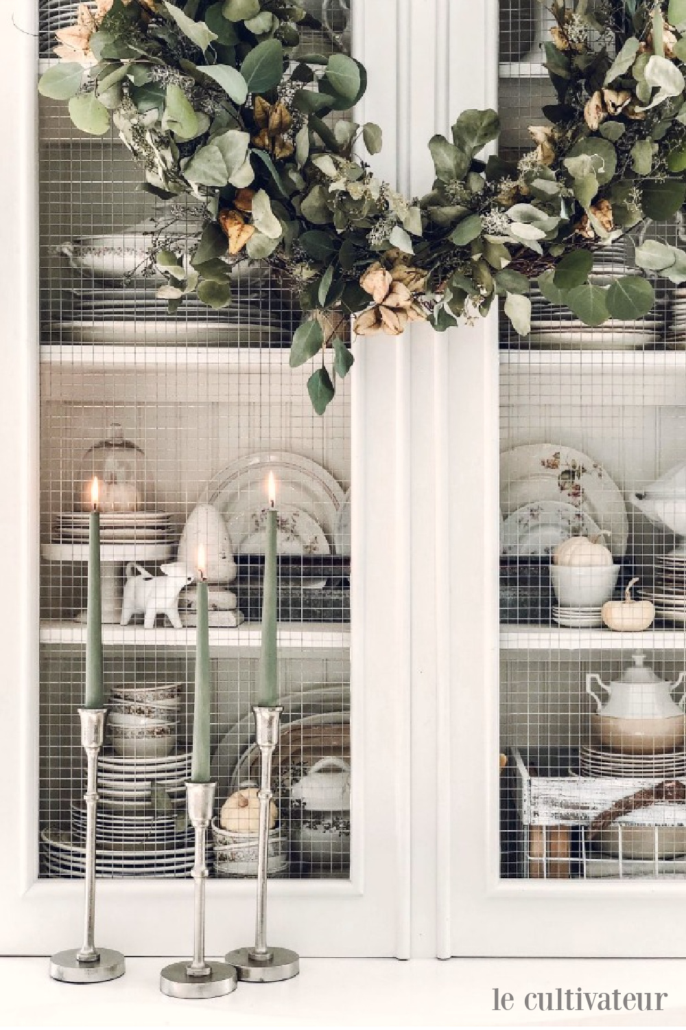 Sage green candles and eucalyptus wreath on a white French country cabinet in a fall vignette - Le Cultivateur. #falldecor #fallwreath #sagegreen