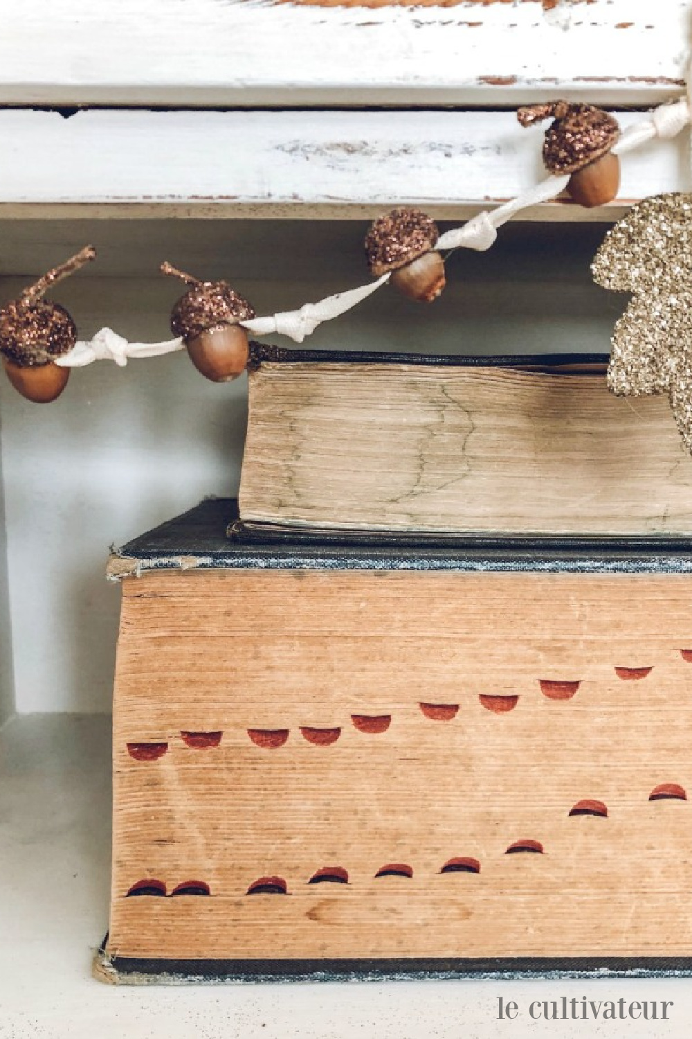 Charming fall acorn garland on a shelf with vintage books sporting aged pages - Le Cultivateur. #acornwreath #falldecor #countrydecor