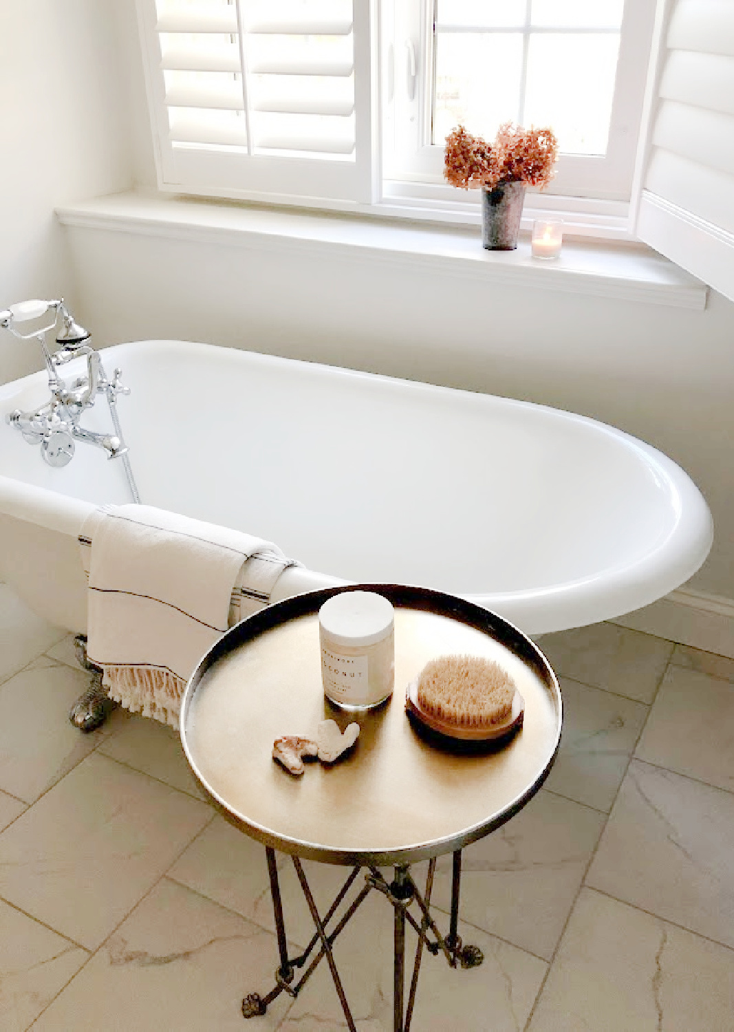 Serene vintage style white bath with clawfoot tub, plantation shutters, and staggered marble tile - Hello Lovely Studio. #serenedecor #serenebath