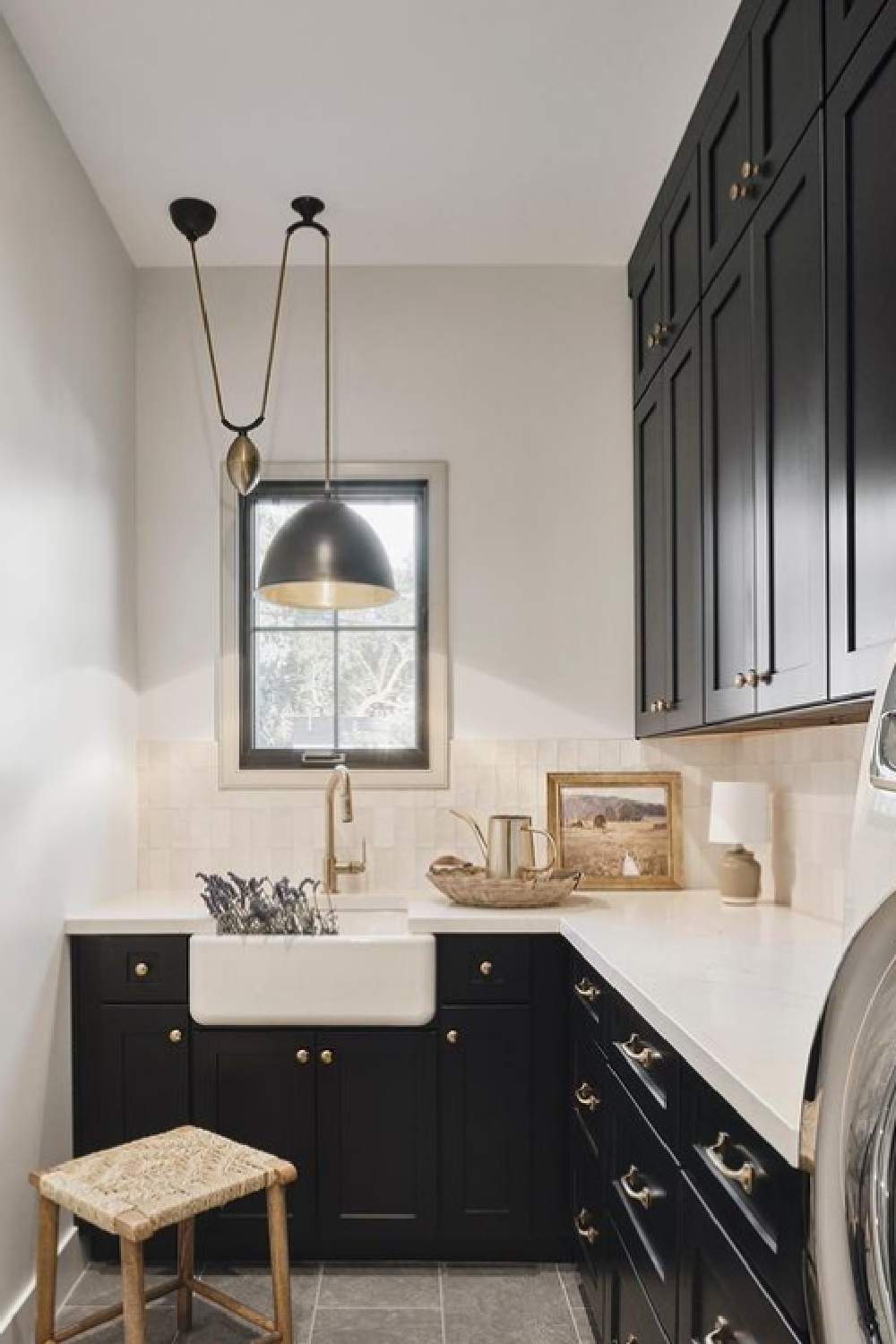 Beautiful black and white laundry room with black cabinets, Zellige tile backsplash pendant over farm sink, and white counters - @_rafterhouse_ #laundryrooms #blackcabinets