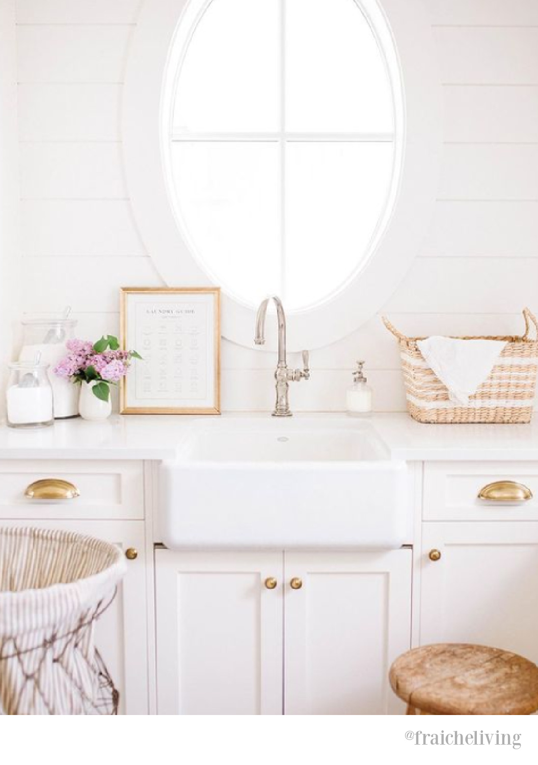 Lovely oval window over farm sink in a white country laundry room by Fraiche Living. #laundryrooms #ovalwindow #farmhouselaundryroom