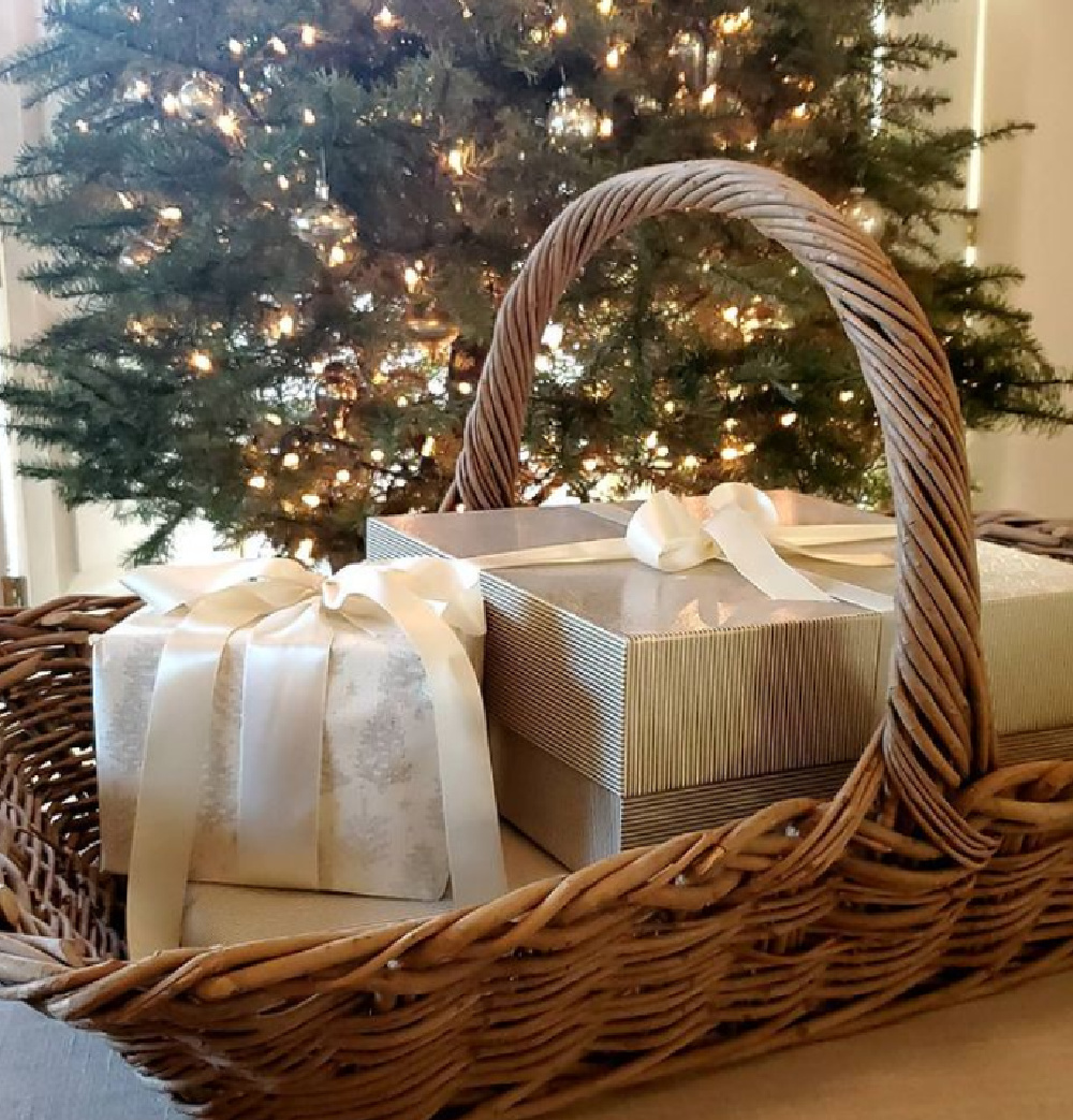 Elegant gifts tied in white ribbon in a French basket near Christmas tree - The French Nest Co Interior Design. #frenchcountrychristmas