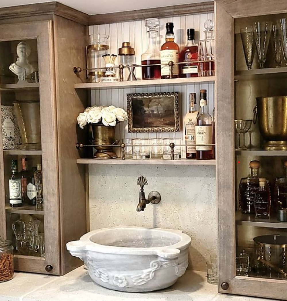 Rustic elegant French country wet bar with stone sink, wall mount faucet, and glass front cabinets - @thefrenchnestcointeriordesign