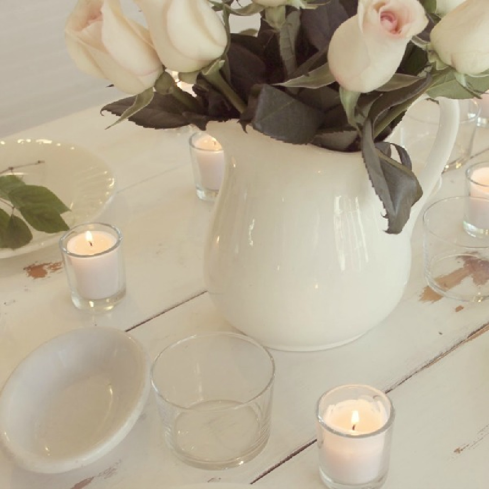 White ironstone pitcher with blush roses on a white  rustic farm table with candles - Hello Lovely.