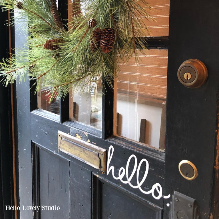 Charming farmhouse front door painted black and handlettered with "hello" is decorated with Christmas wreath at Urban Farmgirl - Hello Lovely Studio. #farmhousechristmas #frontdoor #blackdoor #holidayporch