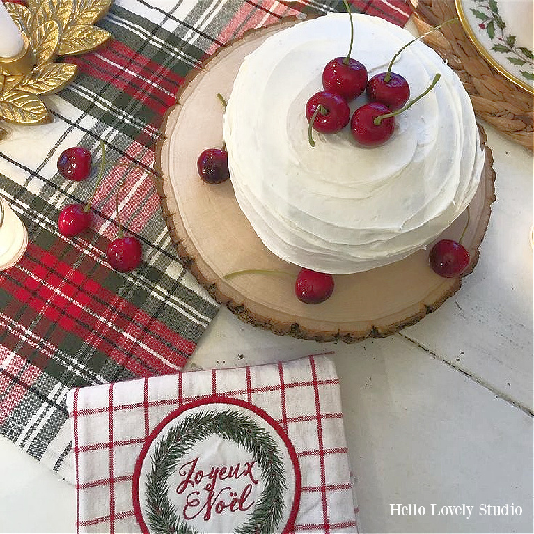 Rustic farmhouse Christmas cake with cherries, plaid table runner, and Joyeux Noel dish towel - Hello Lovely Studio.