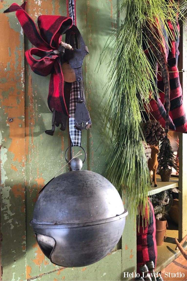 Farmhouse Christmas decor with galvanized large bell hung from ribbon on green vintage door - Hello Lovely Studio. #christmasdecor #christmasbell #farmhousechristmas #vintagechristmas #frontdoordecor