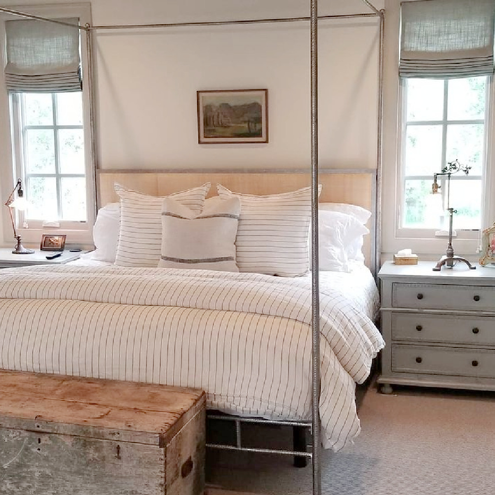 Rustic modern French bedroom with linen roman blinds, poster bed, raw wood trunk, and sumptuous bedding - design by @beljarhome. #serenedecor #modernfrench #europeancountry #bedroomdecor