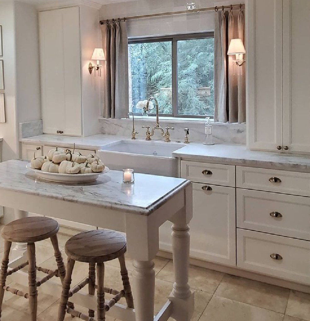 Serene elegant sophisticated white French kitchen with petite island and sconces flanking farm sink - The French Nest Co Interior Design. #whitekitchens #modernfrench