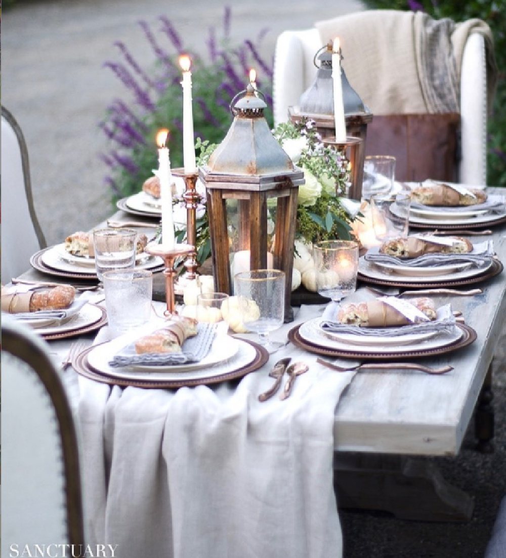 Outdoor Thanksgiving tablescape with French farmhouse style, rustic lanterns, and elegant chairs - @sanctuaryhomedecor. #thanksgivingtable #tablescapes #frenchfarmhouse