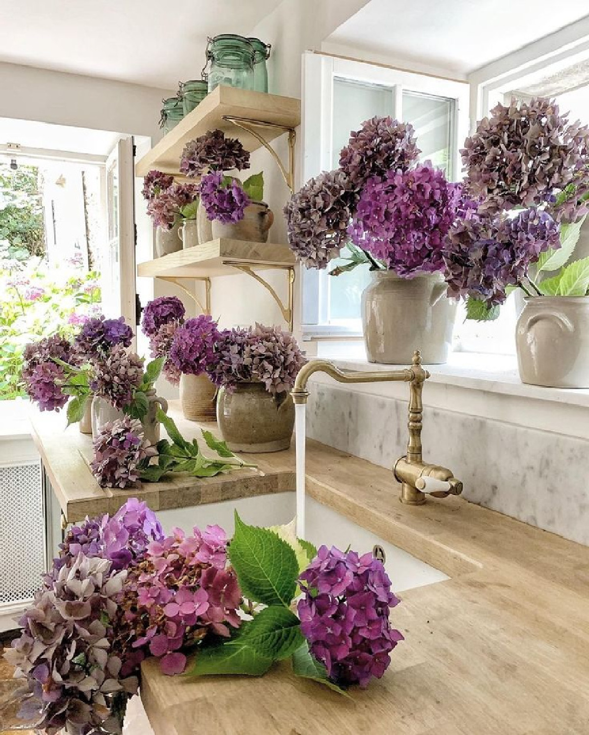 Lovely end of summer purple hydrangeas in a beautiful French farmhouse kitchen with wood countertops - Vivi et Margot. #frenchfarmhouse #frenchcountry #hydrangea #frenchkitchen #countrykitchens #woodcountertop #kitcheninfrance