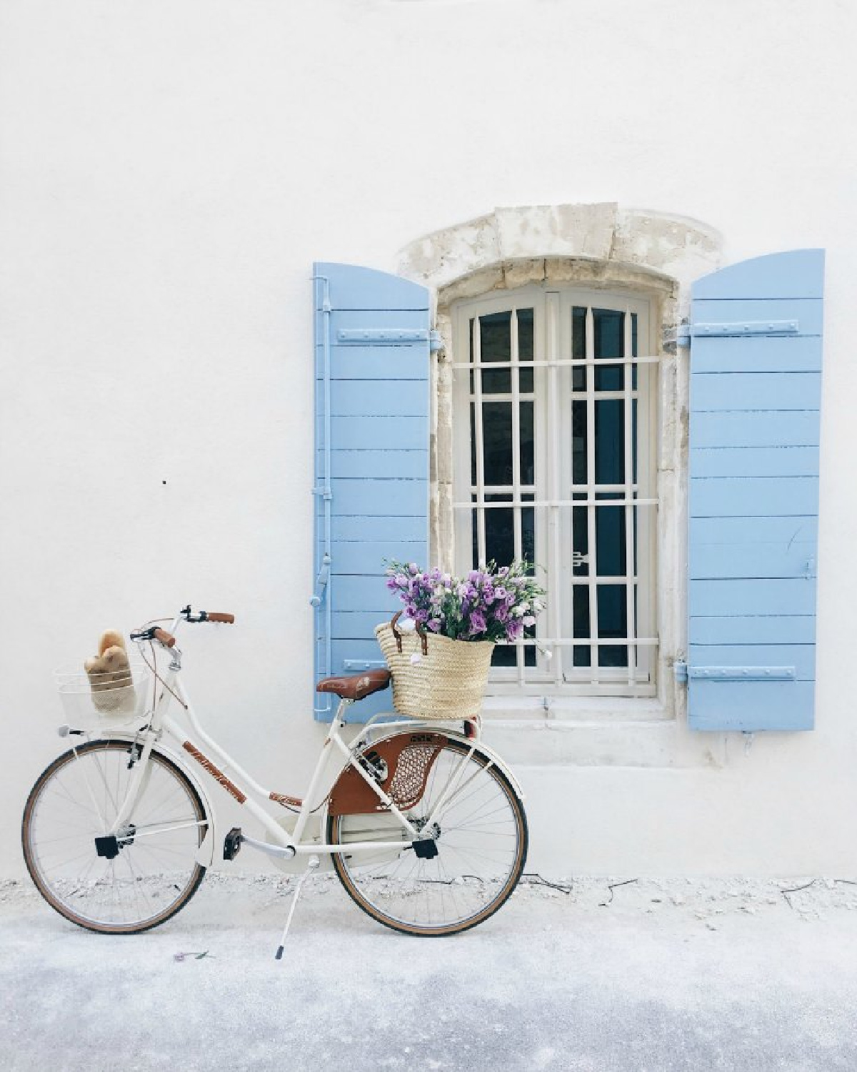 Charming French country vignette with white bicycle, French market basket of flowers, bright blue shutters, and a crisp white house exterior. Romantic indeed! #provencestyle #romanticfrance