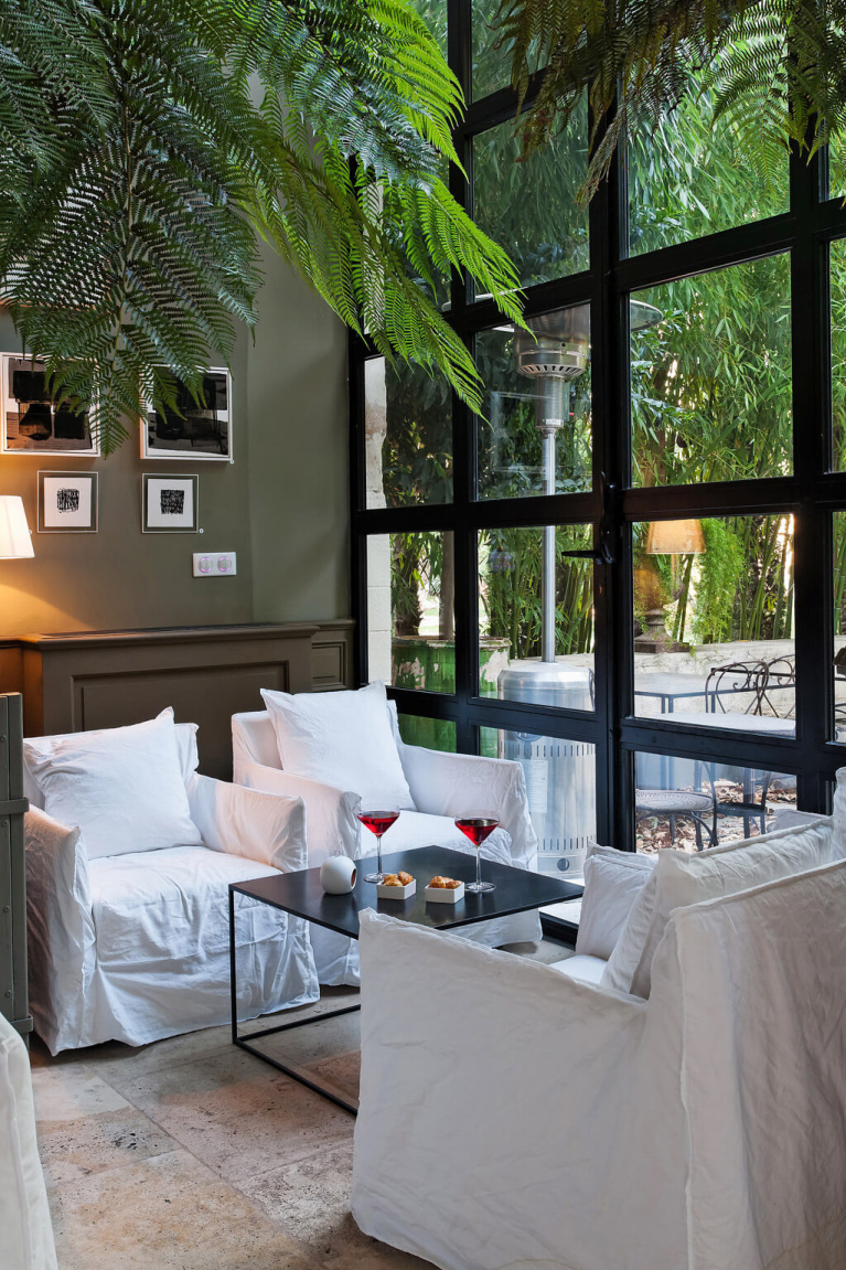 Deep taupe walls and crisp white modern slipcovered chairs in a French lounge area of Avignon Hôtel Particulier, a beautifully restored 19th century mansion in the heart of Avignon’s historic center - Haven In. #modernfrench #frenchcountrydecor #frenchchateau #provence #frenchcountry #restoredchateau #southoffrance #aivgnonhotel