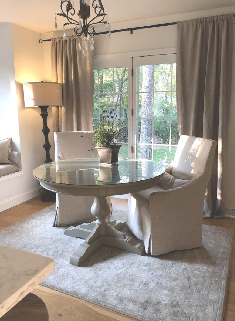 Serene Decor in our breakfast nook with Belgian linen slipcovered chairs, round dining table, and Couristan area rug - Hello Lovely Studio. #hellolovelystudio #breakfastnook #belgianlinen #slipcoveredchairs #cozykitchen #europeancountry #frenchcountrystyle