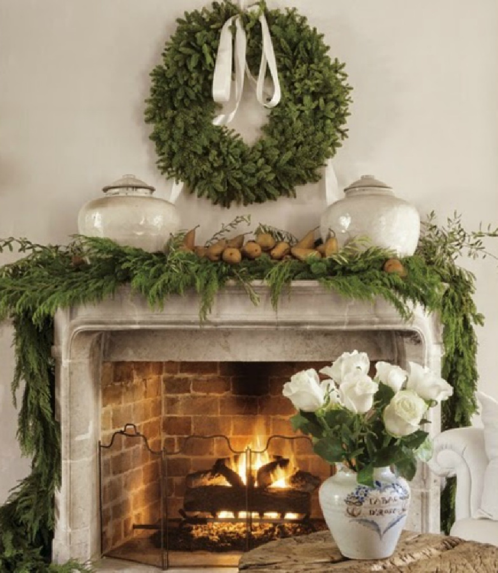 Pamela Pierce decorated Christmas fireplace. A fire is kept in the living room and a French period carved stone mantle and surround has mixed garland and olive branches gathered from trees in her yard, Ripe brown pears look so elegant with  early Song dynasty jars. White roses are always part of Pam’s interior décor.