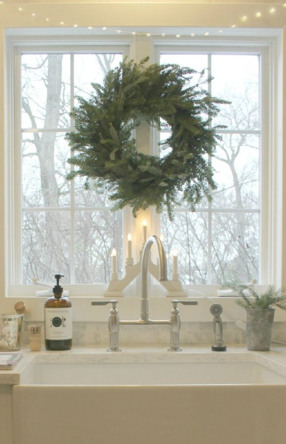 Scandinavian Christmas decor in my white kitchen with Swedish candelabra, fresh fir wreath, and fairy lights over farm sink window. #hellolovelystudio #christmasdecor #swedish #scandinavian #whitechristmas #nordicfrench