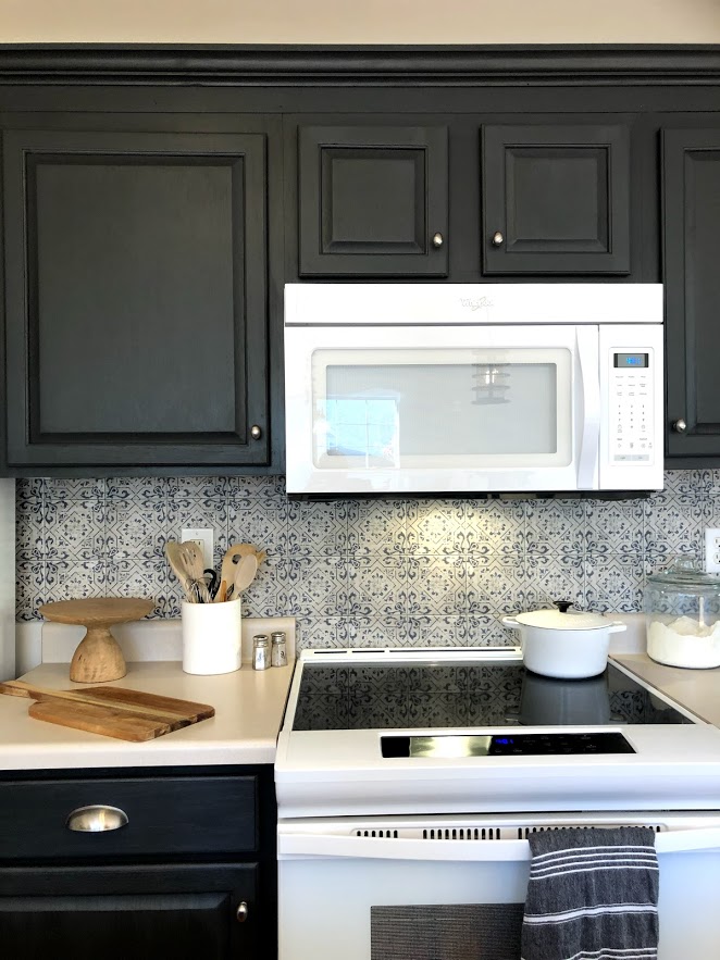 A modern white Whirlpool electric range contrasts with dark gray cabinets and a Spanish tile backsplash.