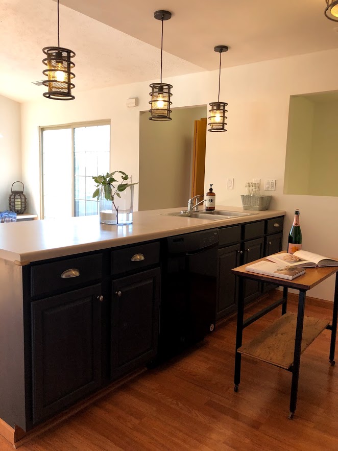 Three industrial style pendant lights over a breakfast bar with cabinets painted Sherwin Williams Carbonized - a deep dark charcoal.