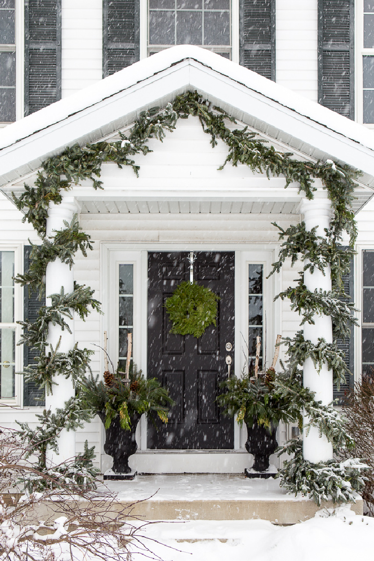 Beautiful white traditional house exterior with black door decorated for Christmas with garland and wreath - Just a Girl Blog.