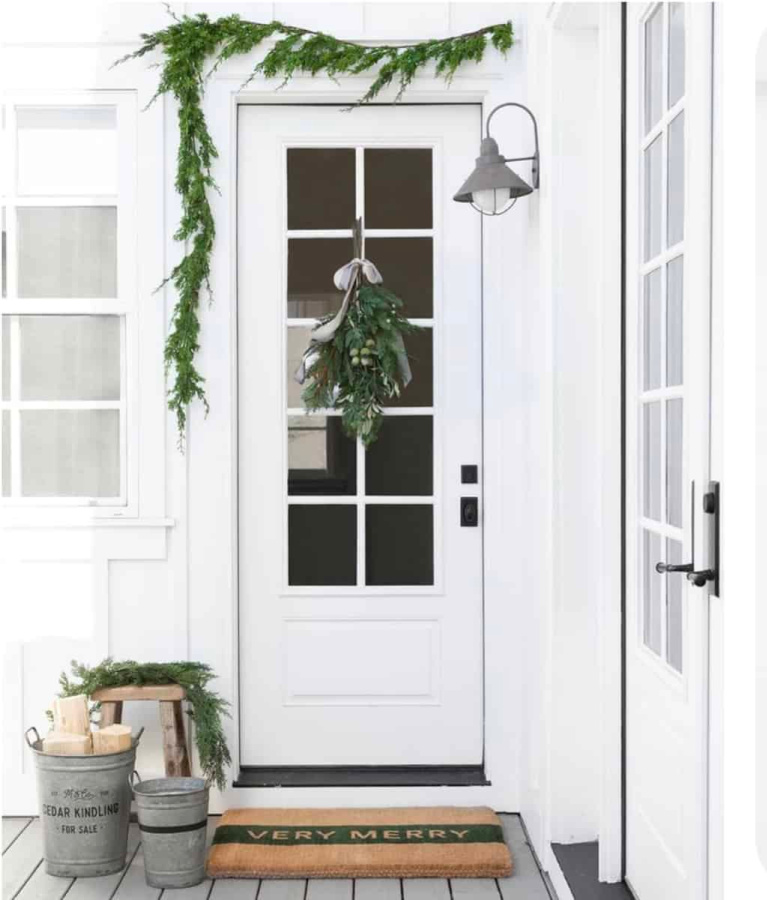 White farmhouse exterior decorated for Christmas simply with fresh greenery, doormat, and galvanized buckets - Studio McGee.