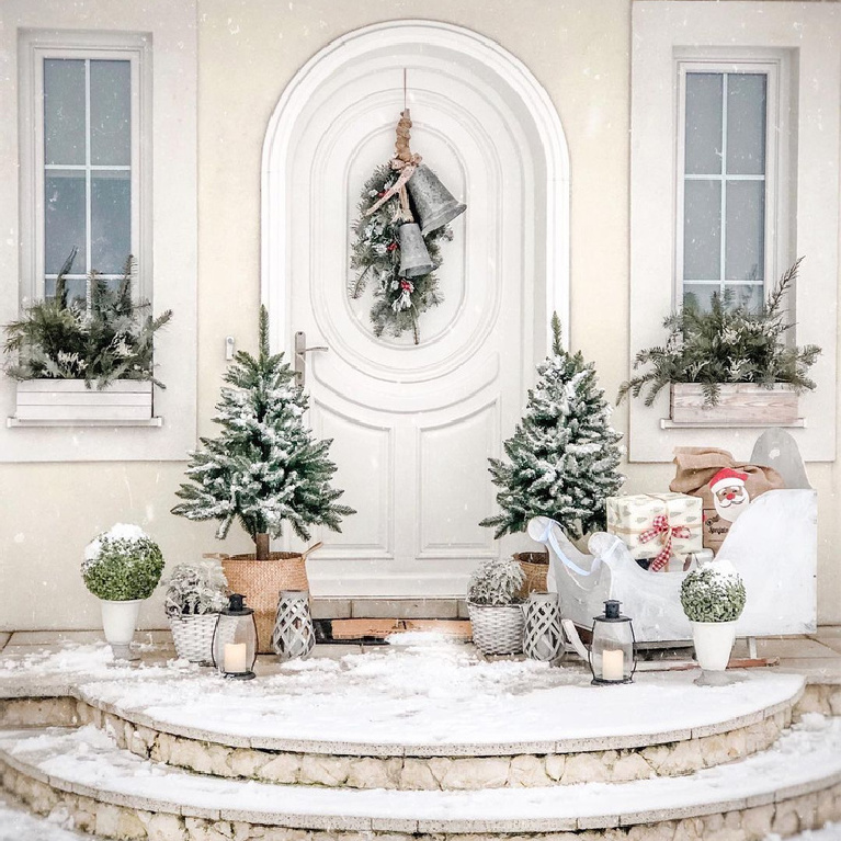 Enchanting home exterior with white arched door and Christmas decorations including bells, greenery in window boxes, and Santa's sleigh - @Basniowy.