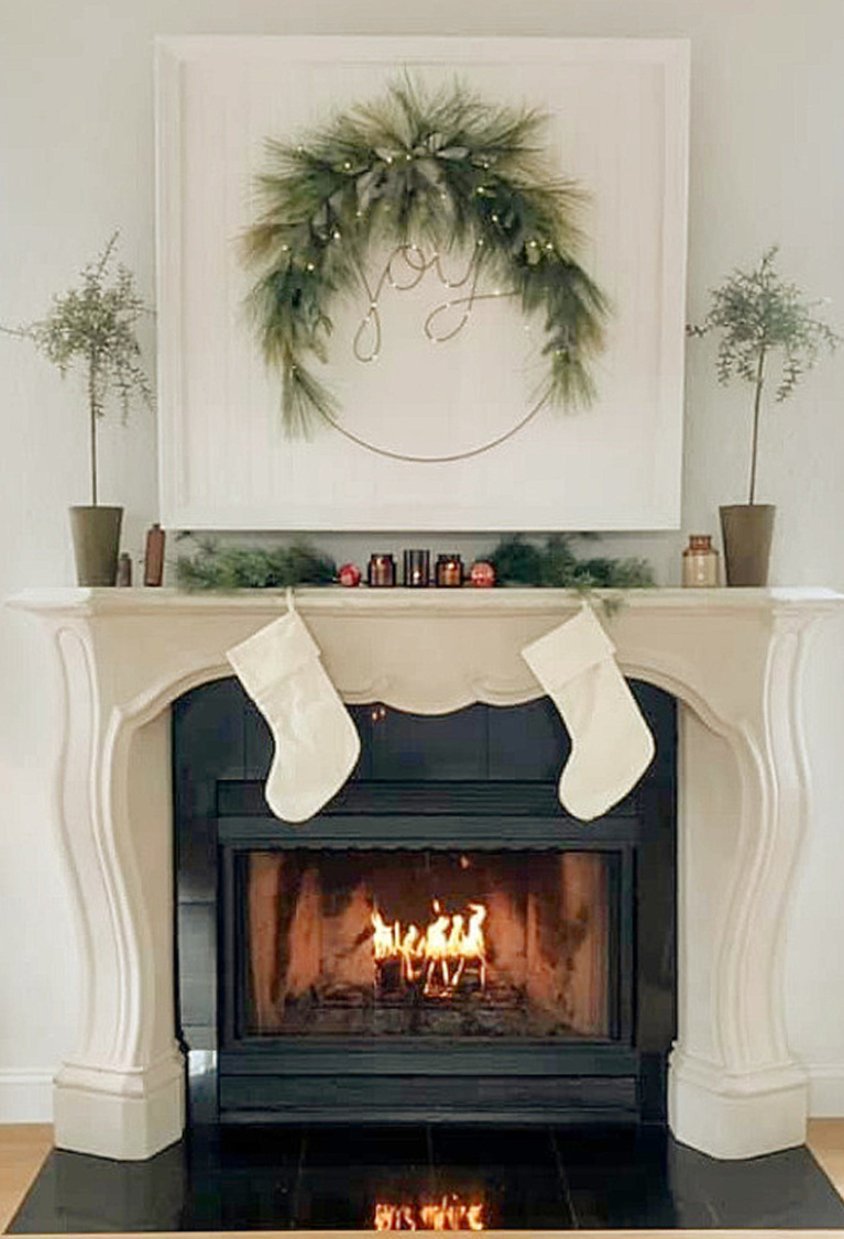 White natural European inspired Christmas decor on fireplace and mantel with joy wreath and stockings - Hello Lovely Studio. #christmasdecor #christmasfireplace #scandichristmas #frenchchristmas