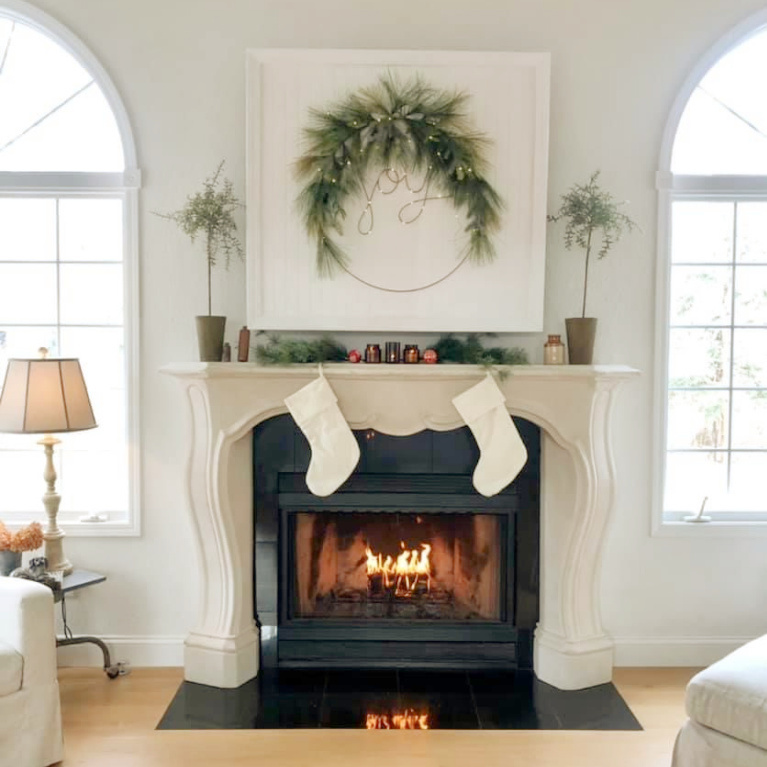 White natural European inspired Christmas decor on fireplace and mantel with joy wreath and stockings - Hello Lovely Studio. #christmasdecor #christmasfireplace #scandichristmas #frenchchristmas