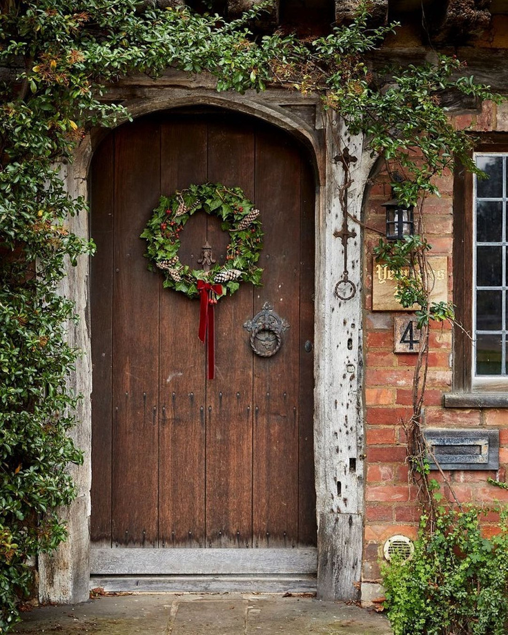 Beautiful cottage with arched wood door hung with Christmas wreath - @hunt_the_pearl.