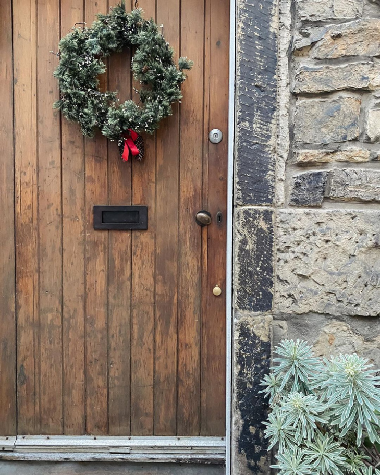 Charming Christmas wreath on an old planked wood door of a stone cottage - @home_stead