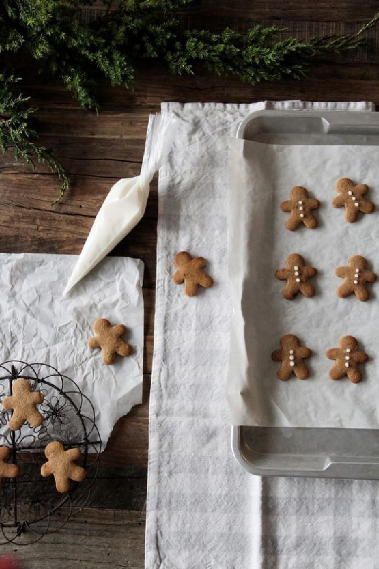 Charming flatlay image of mini gingerbread men cookies on a rustic farm table being iced simply - Scandinavian style Christmas decor beauty - ForkandFlower.