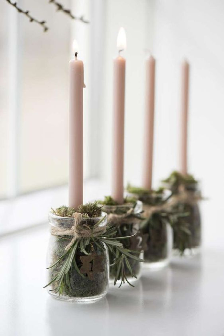 Simple Scandinavian Christmas decor idea with little glass jars of moss to hold candles and sprigs of rosemary tied with twine at top. #scandinavianchristmas #tablescape #candleholders