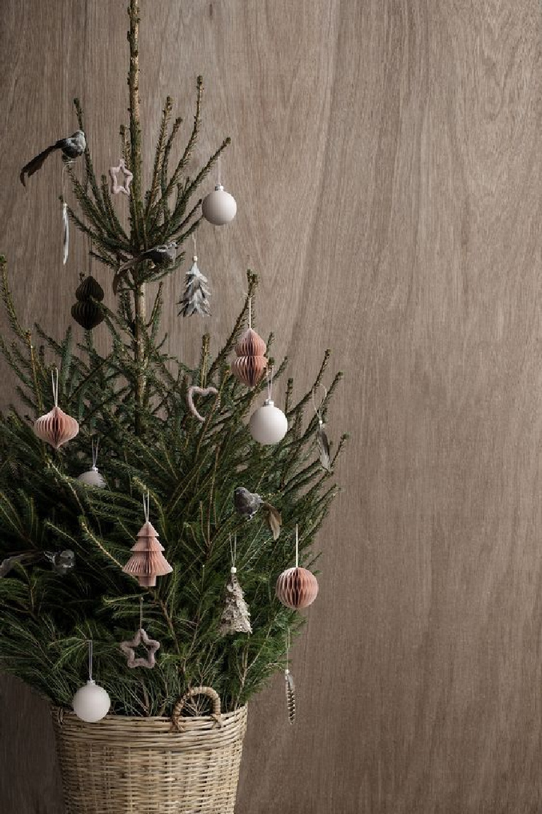 Scandinavian Christmas decor - a small fresh Christmas tree in handled basket with paper ornaments looks modern and serene against a wood backdrop - Bloglovin.