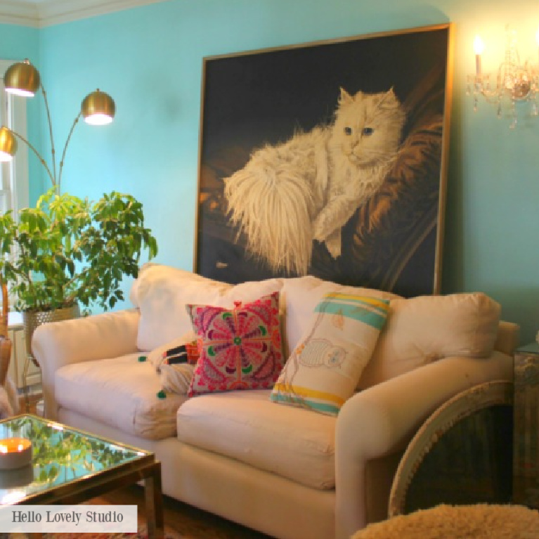 A large vintage cat portrait hangs above a traditional white sofa in a colorful living room reflecting Grandmillennial style - Jenny Sweeney design on Hello Lovely.