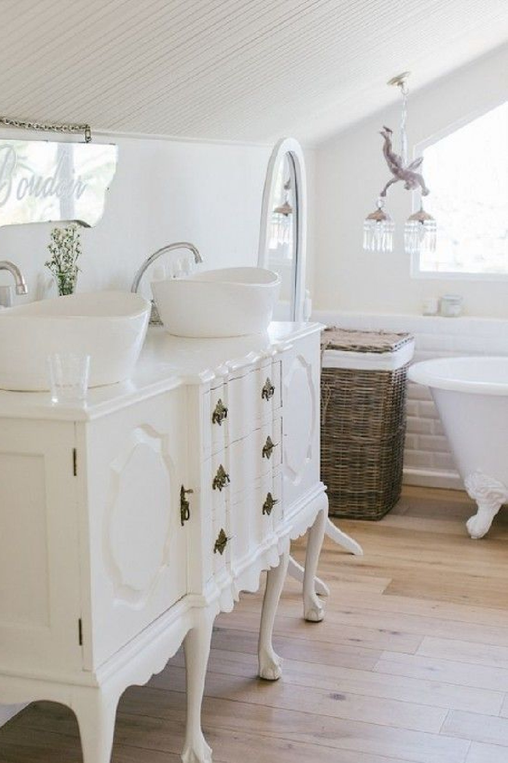 A repurposed dining room buffet is painted white and used as a bathroom vanity with vessel sinks. in a cottage style bathroom. Come check out Antique Vintage Style Bathroom Vanity Inspiration! #bathroomdesign #bathroomvanity #classicstyle #traditionaldecor #interiordesignideas