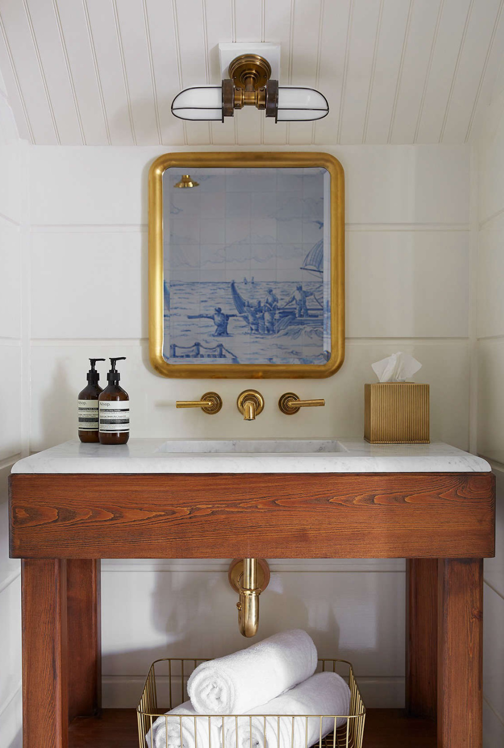Showers are lined in maritime scenes made of Portuguese tiles, and sconces on the eaves have an air of recycled industrial corridor lights. The boxy and unpainted sink vanities, reminiscent of 19th-century farmhouse washstands, leave glossy pipes exposed.