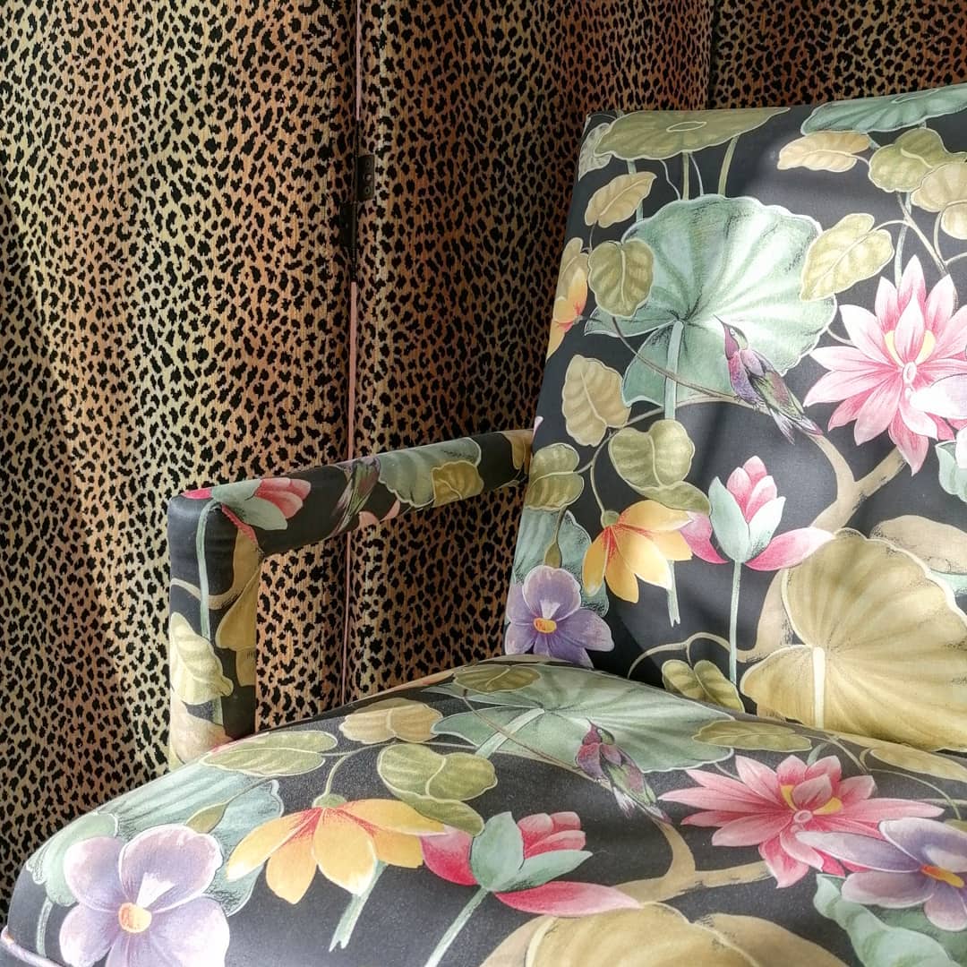 1980s colorful print upholstered arm chair with floral and hummingbirds against an animal print drape - @sideshowinteriors.